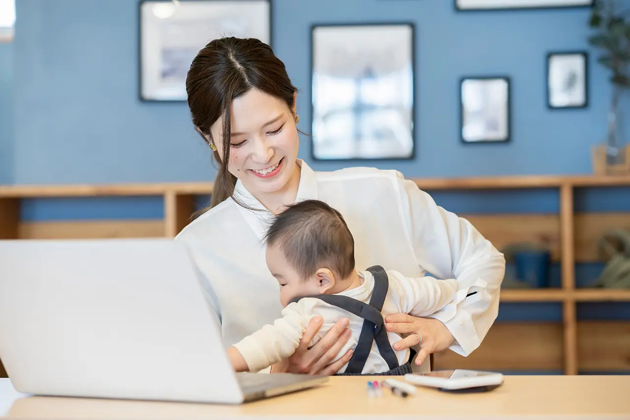 ノートパソコンの前で赤ちゃんを抱っこする母親
